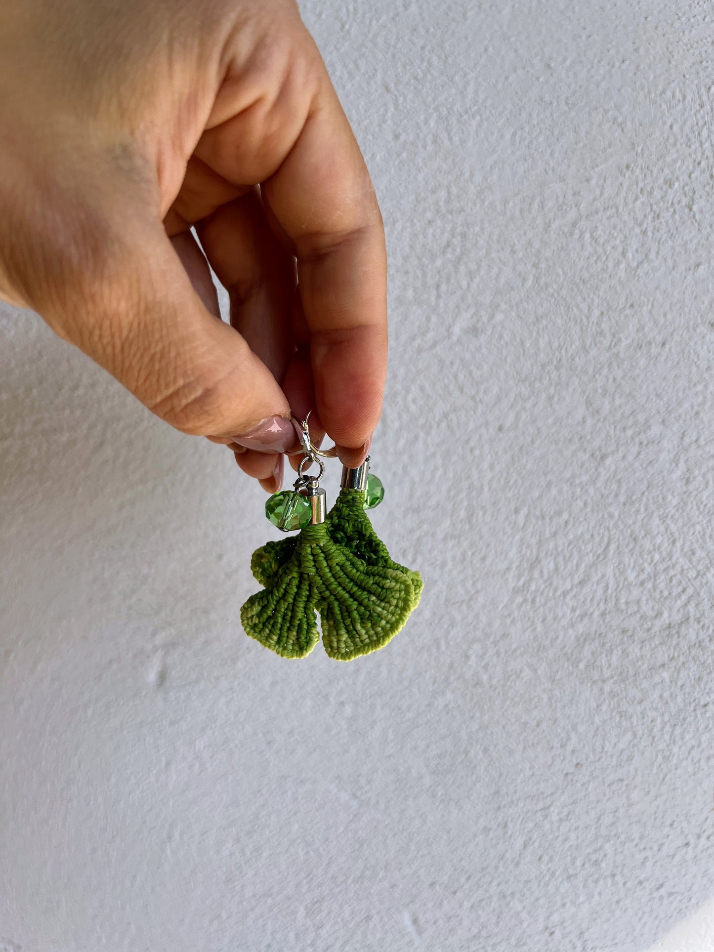 orecchini gingko biloba verdi in mano sfondo muro bianco